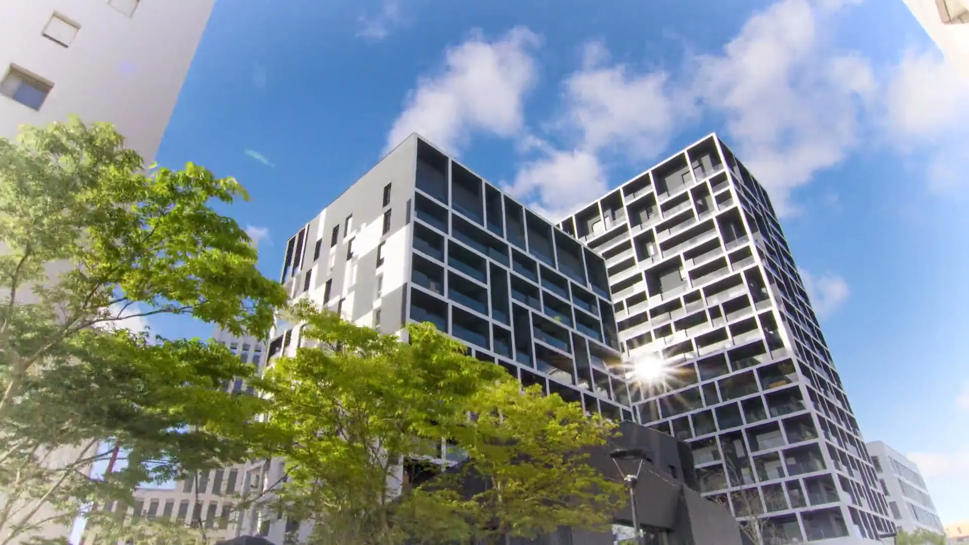 Immeubles de logements en contre-plongée sous un ciel bleu, le soleil se reflète dans une vitre